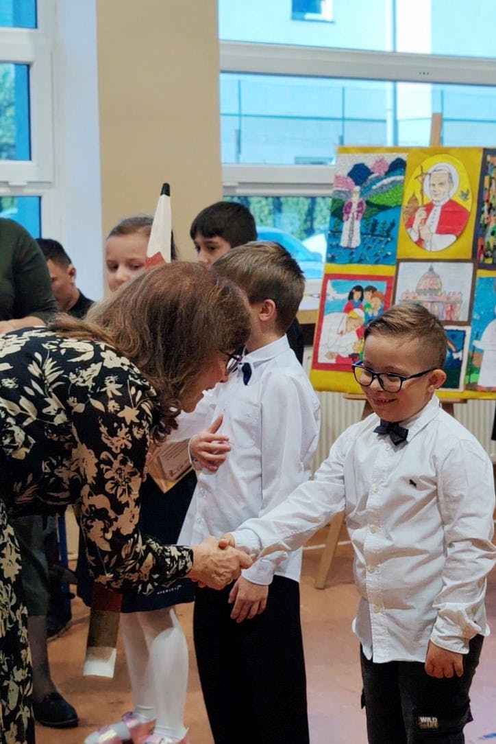 DZIEŃ PAPIESKI | Pani dyrektor gratuluje chłopcu poprzez uścisk dłoni.jpg