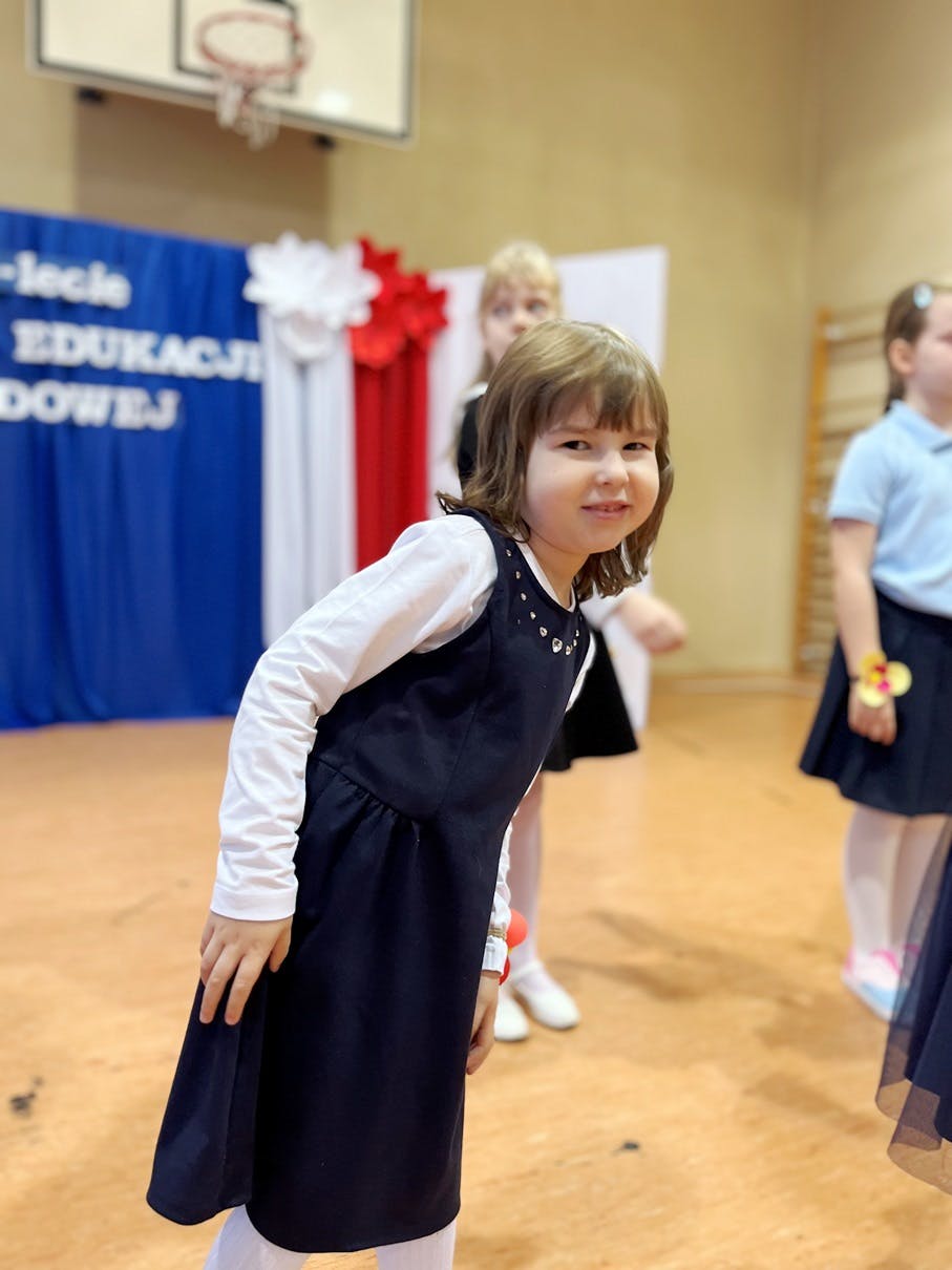 Świętujemy Dzień Edukacji Narodowej | Uśmiechnięta dziewczynka w biało-granatowym stroju uśmiecha się do zdjęciam .JPG