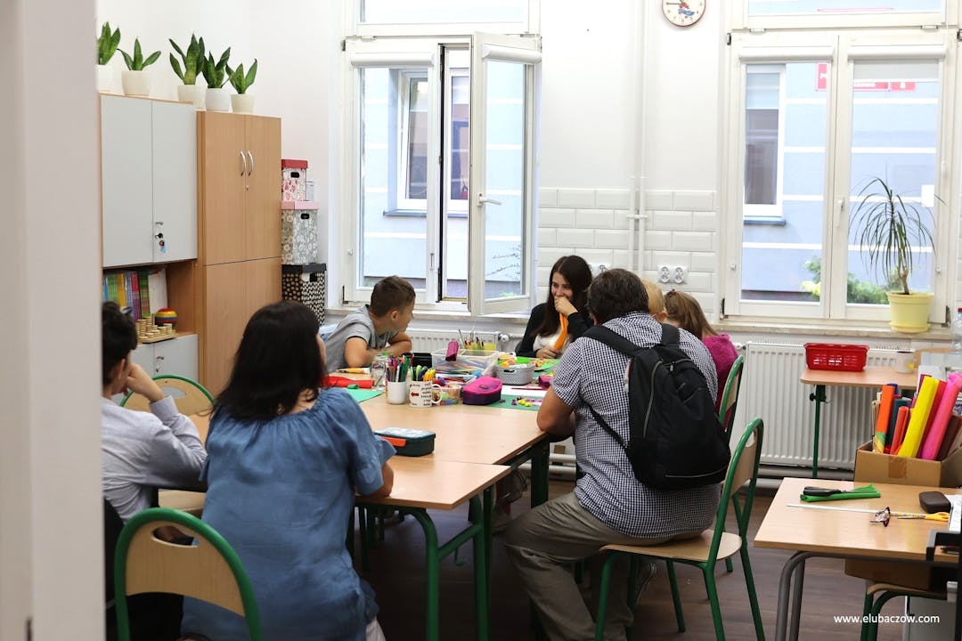 „Przyjazna przystań” | Nauczyciel razem z uczniami siedzą przy stoliku w klasie.jpg