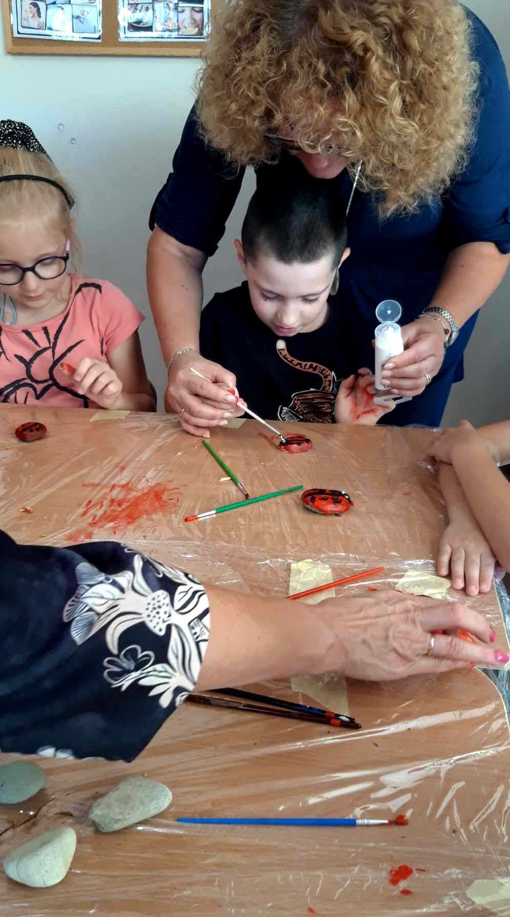 Integracyjne zajęcia w "Krainie uśmiechu" | Nauczyciel pomaga dziecku malować kamień.jpeg