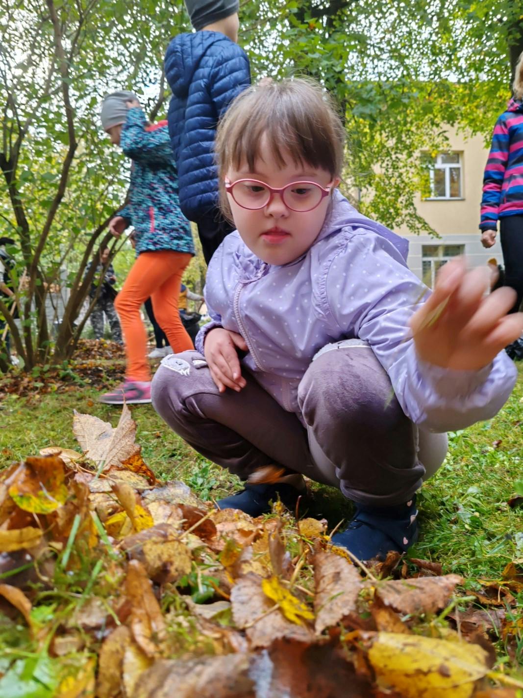 Jesienne prace w ogrodzie | dziewczyna w okularach kuca przy jesiennych liściach.jpg