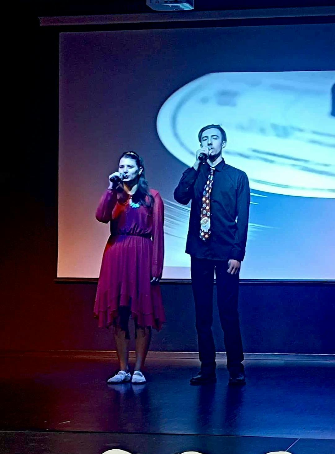 I miejsca dla chóru szkolnego „Karolus” | Dziewczyna i chłopak z mikrofonami na scenie.jpg