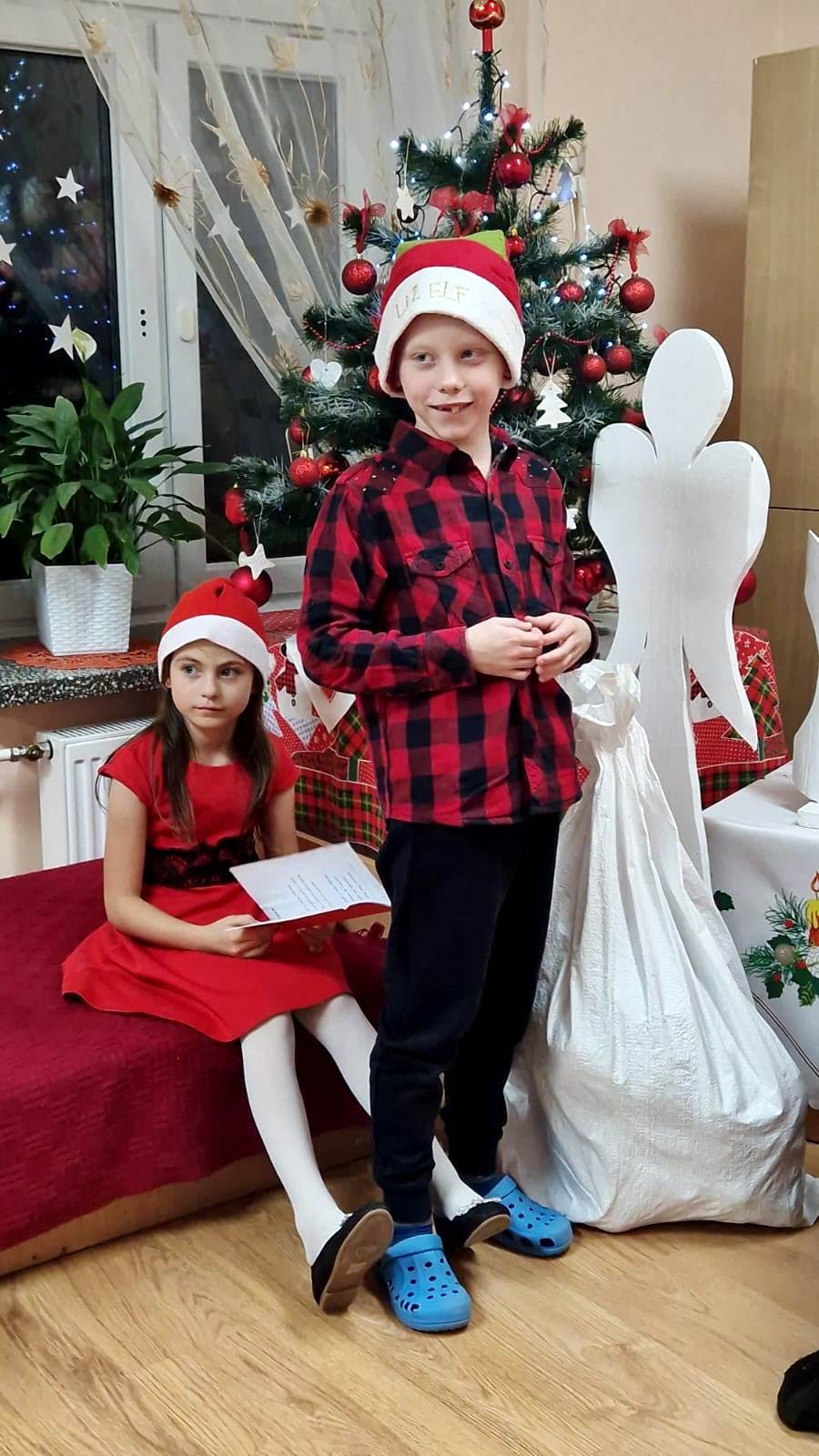 Niezapomniane spotkanie z Mikołajem! | Chłopiec stoi w czerwonej czapce, obiok siedzi dziewczynka .jpg