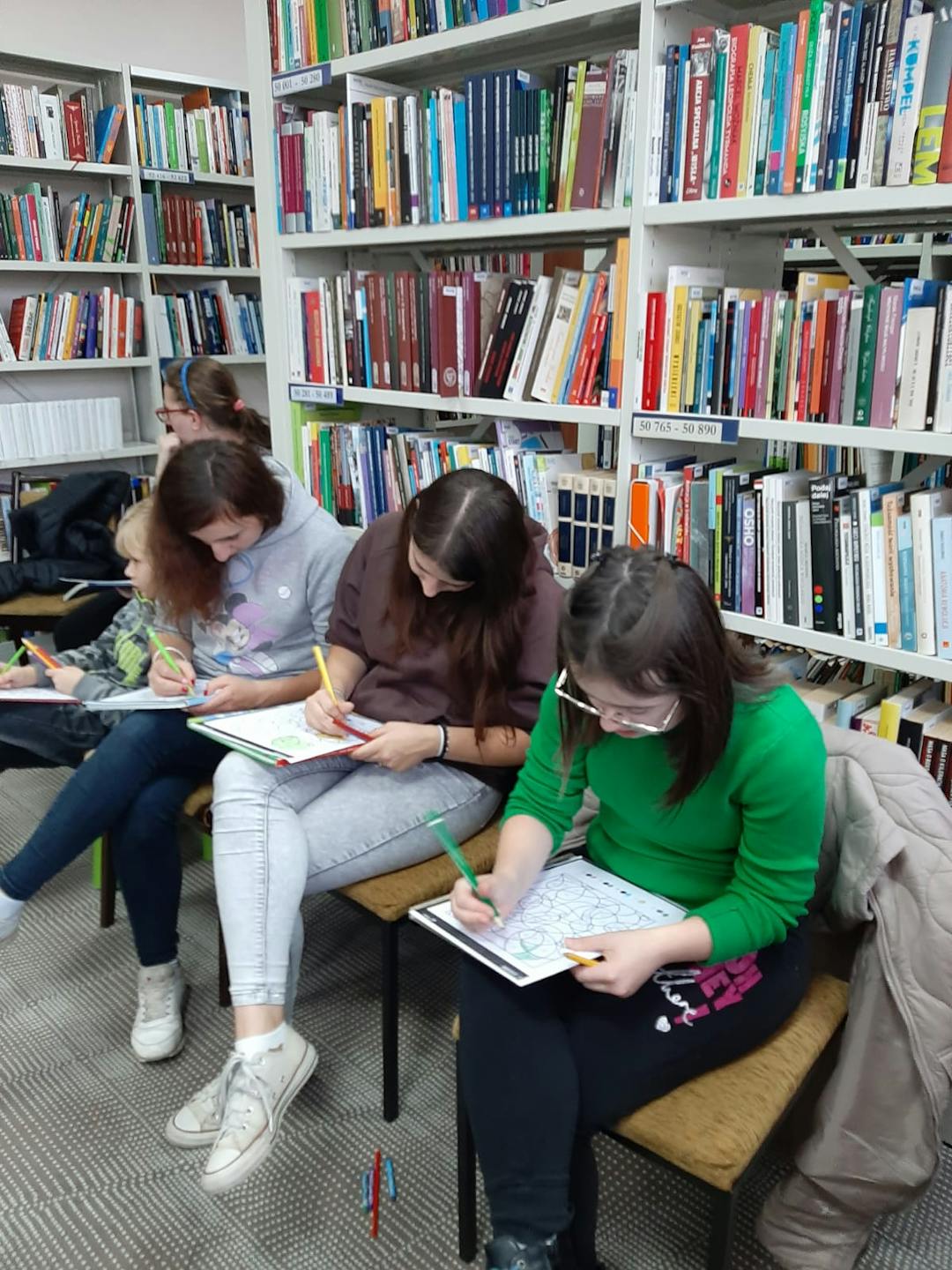 Pozalekcyjne zajęcia w bibliotece | dziewczyny siedzą na krzesłach i koloruja obrazki.jpg