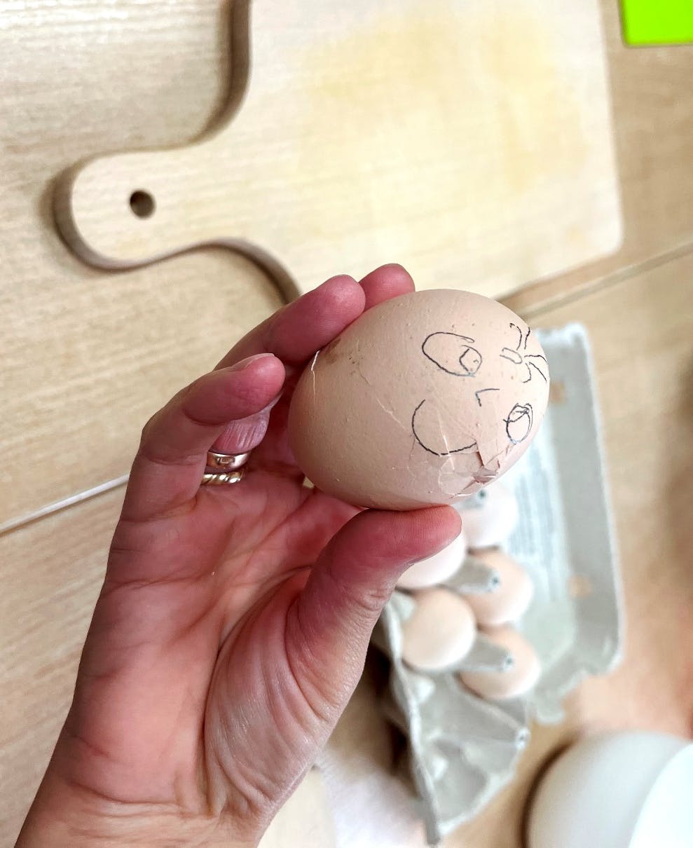 "Zdrowie na jesiennym talerzu" | Na pierwszym planie ręka z trzymająca jajko z namalowaną buzią.JPG