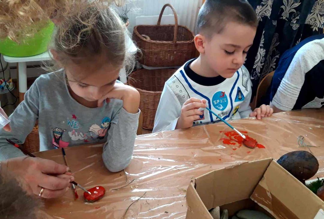 Integracyjne zajęcia w "Krainie uśmiechu" | Dwoje dzieci przy stoliku malują kamienie na czerwono.jpeg