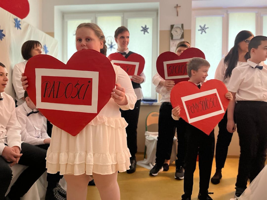 Między światłem, a ruchem… | Uczniowie podczas występu trzymają czerwone serca z życzeniami.jpg