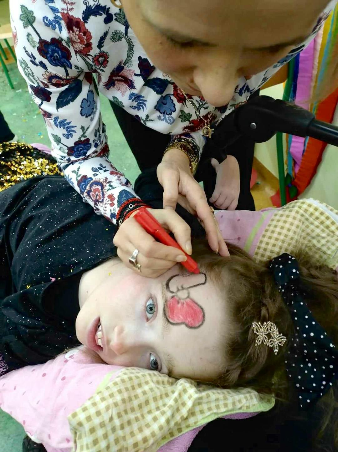 Karnawałowe spotkania | Nauczyciel maluje dziewczynce kokardę na buzi.jpg