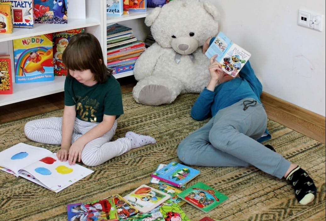 Zrób sobie przerwę na czytanie | Dziewczynka siedzi na dywanie i ogląda książeczkę. Chłopiec leży na dywanie i trzyma w rękach otwartą bajkę. W tle regał z książeczkami_.JPG