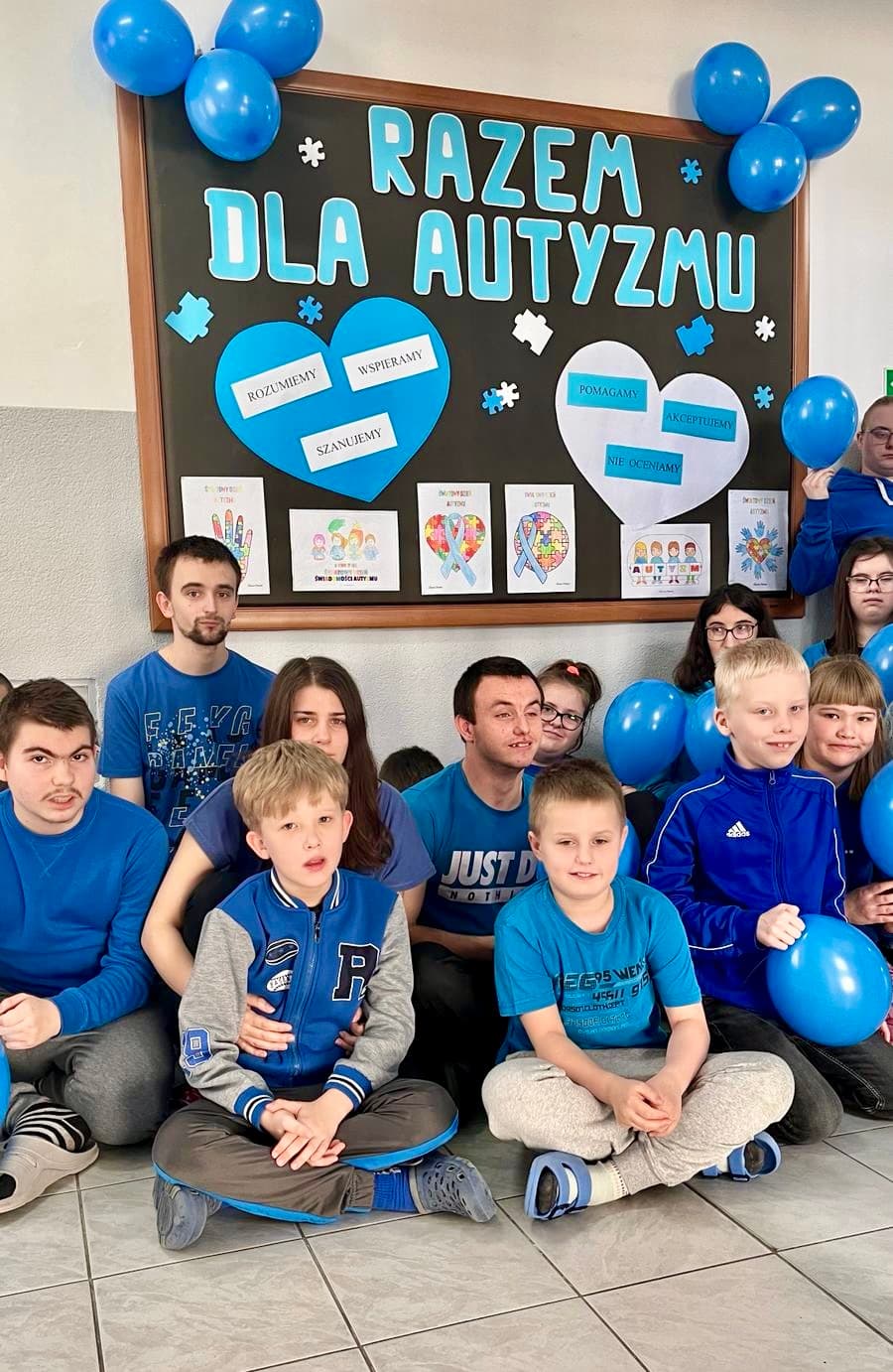 Światowy Dzień Świadomości Autyzmu | Uczniowie ubrani na niebiesko siedzą pod tablica na temat autyzmu.jpg