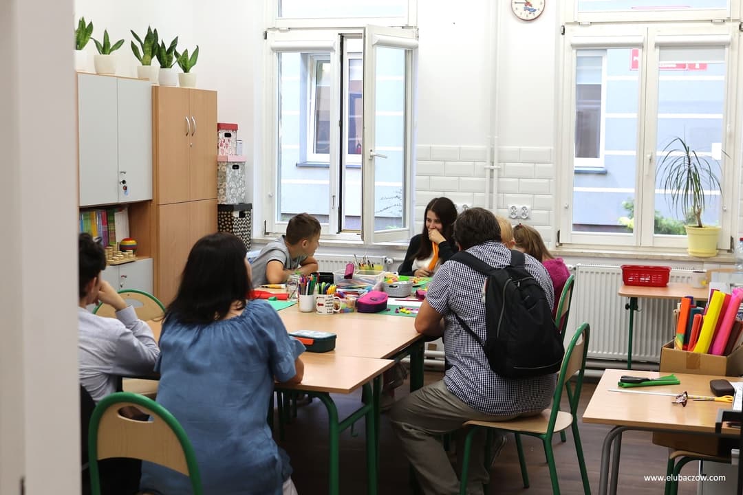 „Przyjazna przystań” | Nauczyciel razem z uczniami siedzą przy stoliku w klasie.jpg