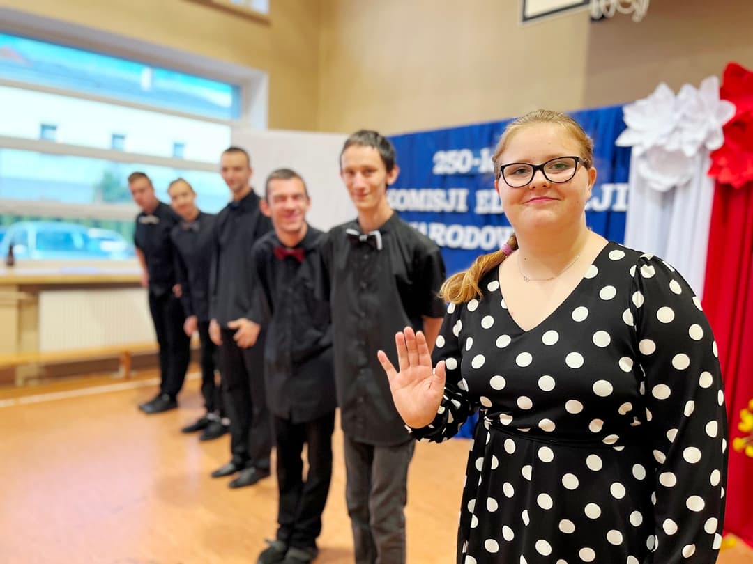 Świętujemy Dzień Edukacji Narodowej | Uczennica macha do zdjęcia, w tel uczniowie w czarnych koszulach.JPG