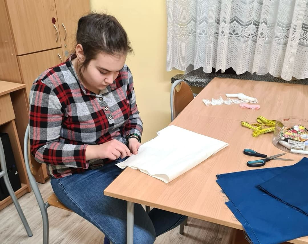 Zajęcia krawieckie w internacie | GŁÓWNE Uczennica szyje materiał przy stole .jpg