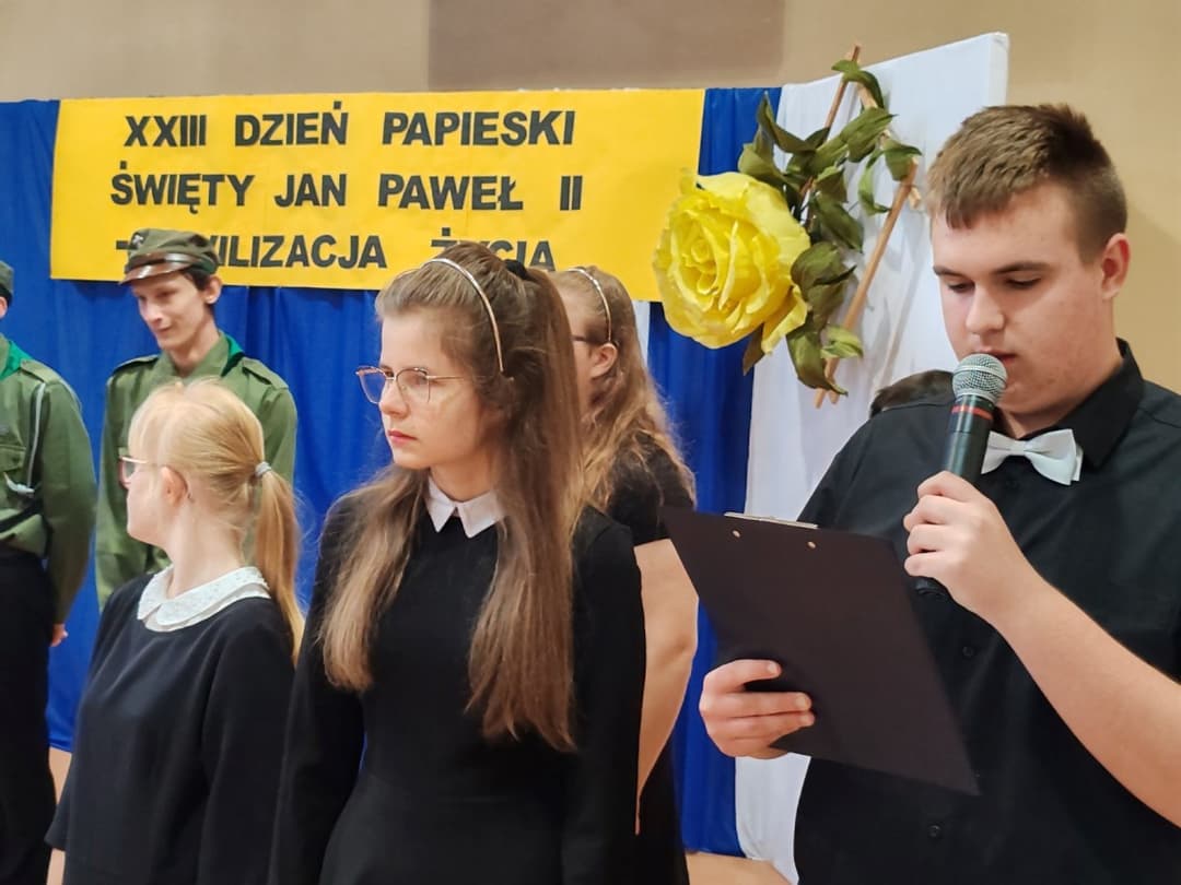 DZIEŃ PAPIESKI | Uczeń czyta do mikrofonu na scenie.jpg