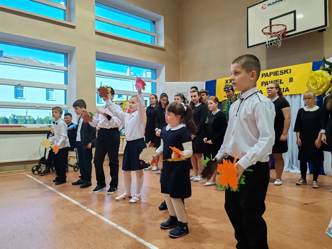 DZIEŃ PAPIESKI | Uczniowie tańczą na scenie z listkami w rękach.jpg