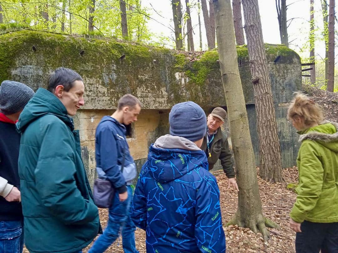 Wyprawa szlakiem bunkrów II wojny światowej | Uczniowie stoją przed bunkrem z przewodnikiem.jpg