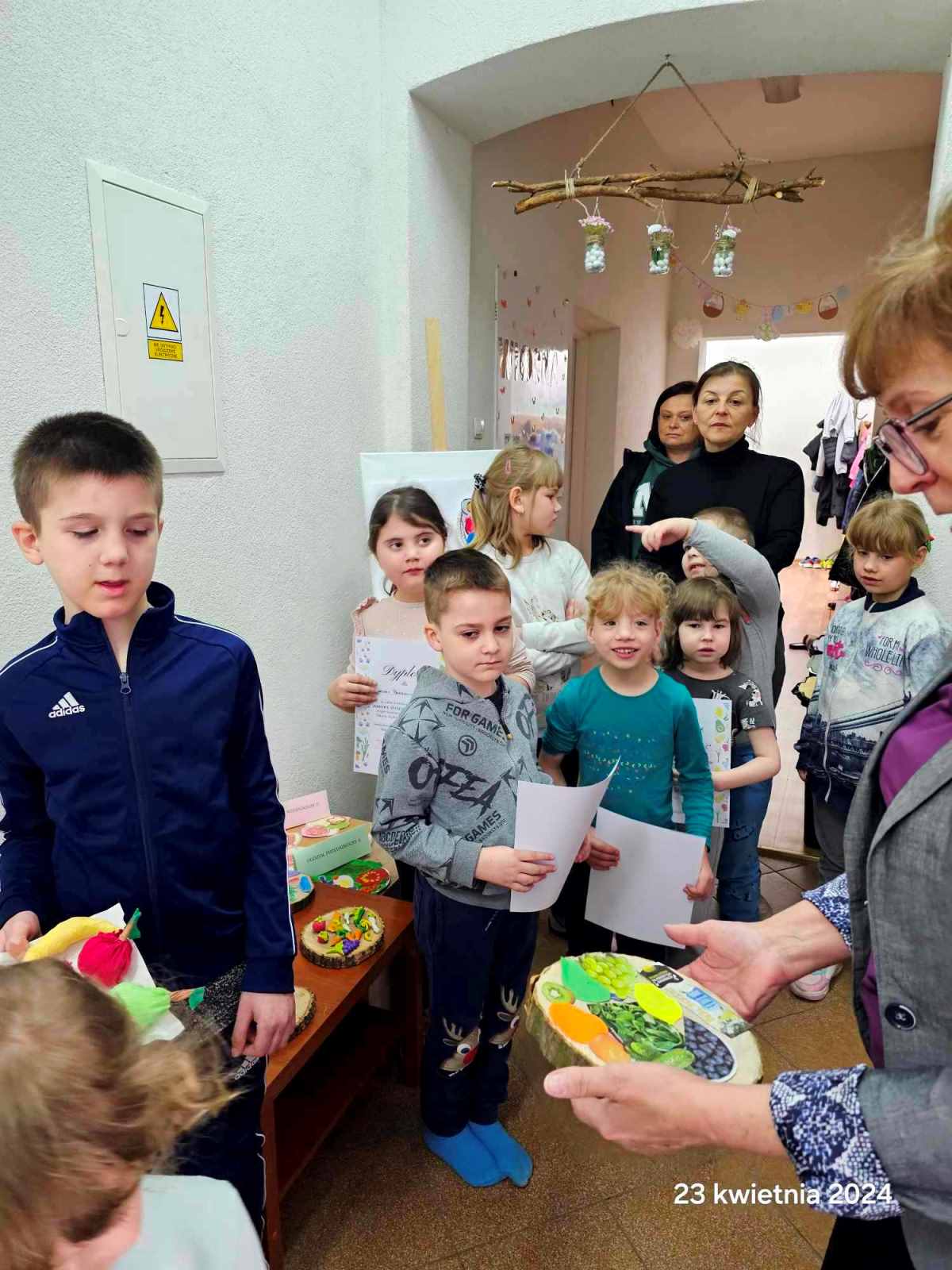 „My, przedszkolaki, zdrowo się odżywiamy i o kondycję dbamy!” | 12 dzieci stoją i tzrymają dyplomy w rękach, Pani Dyrektor ogląda pracę plastyczną.jpg